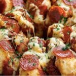 Enjoy a delicious Pizza Monkey Bread, a pull-apart treat topped with melted cheese, pepperoni slices, and fresh herbs. This delightful creation is displayed on a black round baking dish, perfect for any occasion.