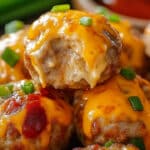 Close-up of a plate of easy party appetizer sausage balls with Rotel, topped with melted cheese and garnished with chopped green onions. A drizzle of barbecue sauce adds a touch of reddish color, enhancing their appetizing appearance.