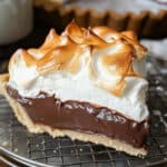 A classic chocolate meringue pie with a creamy dark chocolate filling and golden crust sits on a wire rack, topped with fluffy, browned meringue. This easy chocolate pie recipe offers a delicious dessert presentation.