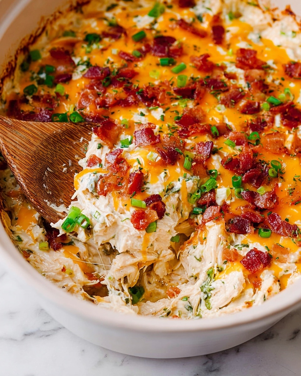 The image shows a creamy mix of shredded white chicken combined with melted orange cheese chunks, speckled with green herbs and small bits of red peppers throughout. The mixture sits in a large white bowl with a spoon on the right side, partially submerged in the thick texture. The background surface is white marble, adding a clean and bright feel to the image. The chicken and melted cheese blend together looking rich and soft, with some herbs adding fresh green contrast. photo taken with an iphone --ar 4:5 --v 7