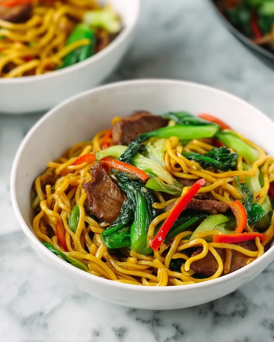 A white bowl filled with yellow noodles mixed with slices of brown cooked meat, bright green vegetables, and thin strips of red and orange peppers. The noodles and ingredients are layered together tightly, with the green vegetables and red peppers adding bright color on top and sides. The background and surface are white marble with subtle gray veins. Another white bowl with similar noodles and vegetables is blurred in the background. Photo taken with an iphone --ar 4:5 --v 7