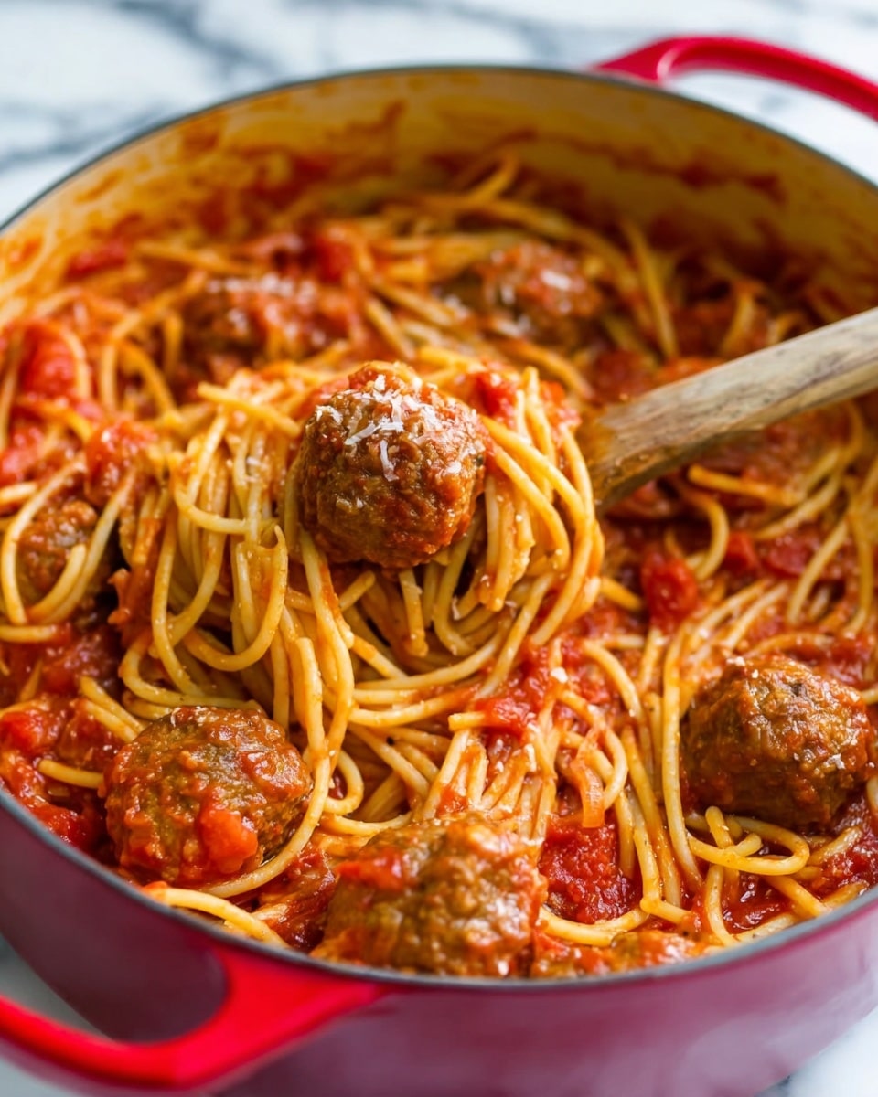A close-up view of a red pot filled with spaghetti and meatballs mixed in a rich red tomato sauce, with visible chunks of tomato scattered throughout. The spaghetti noodles are light golden yellow and slightly glossy from the sauce, swirling around several medium-sized brown meatballs coated in sauce. A wooden spoon is lifting two meatballs and some noodles from the pot. The background shows a white marbled surface. Photo taken with an iphone --ar 4:5 --v 7