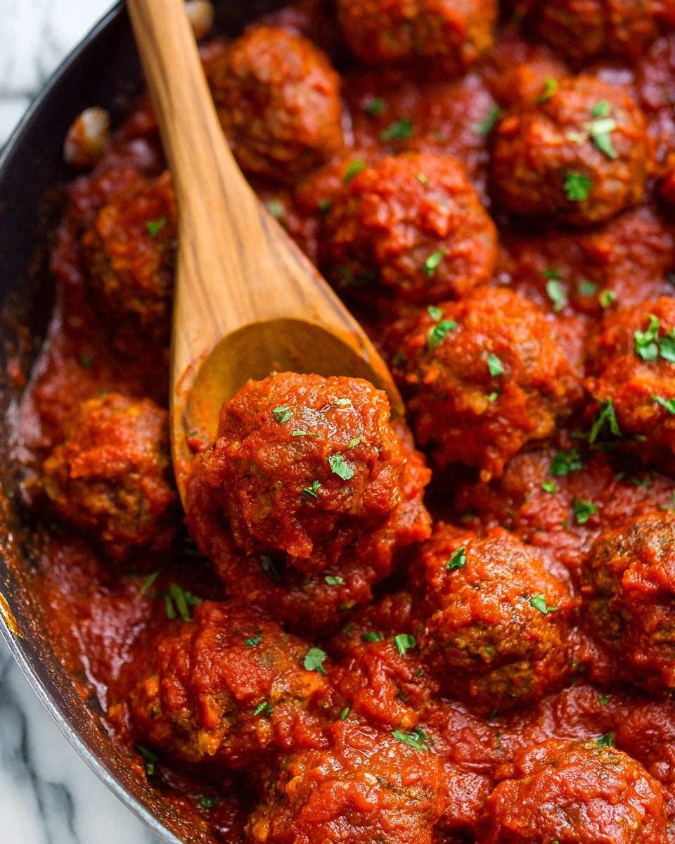 The image shows many round meatballs covered with a thick red tomato sauce, arranged close together in a pan. The meatballs have a slightly rough texture and are garnished with small green herb pieces scattered on top. A wooden spoon is lifting one meatball, revealing its shape and sauce coating clearly. The background has a white marbled texture. photo taken with an iphone --ar 4:5 --v 7