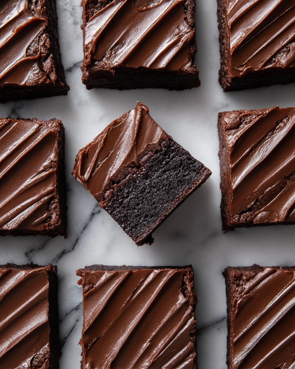 A square white baking dish lined with parchment paper holds a rich, dark chocolate dessert with a smooth and shiny ganache topping. The ganache has diagonal swipe marks across the surface, adding a textured look with waves and ridges. The dish is set on a white marbled surface with a beige textured cloth partially visible underneath the dish. The edges of the parchment paper are slightly folded inside the dish, showing the thickness of the dessert beneath the glossy chocolate layer. photo taken with an iphone --ar 4:5 --v 7