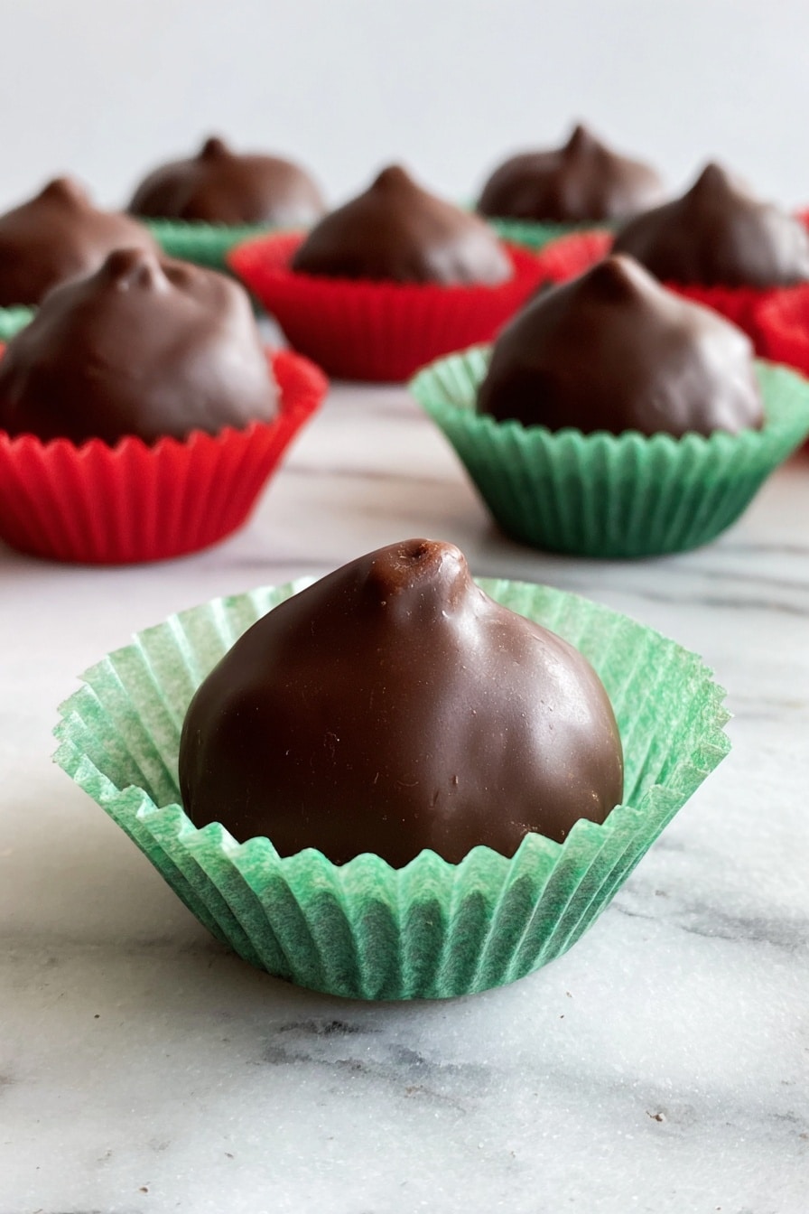 A group of small round chocolate-covered treats sits on a white marbled surface, each resting in a crinkled paper cup. The closest treat is in a green paper cup, showing a smooth, shiny dark brown chocolate coating with a small peak at the top. Behind it, several more chocolates are in red and green paper cups, all similar in shape and texture, creating a neat cluster. The soft light highlights the glossy finish of the chocolates against the white marbled background. photo taken with an iphone --ar 2:3 --v 7 - Chocolate Covered Cherry Delights, cherry cordial candies, homemade cherry chocolates, chocolate dipped cherry treats, classic cherry confections