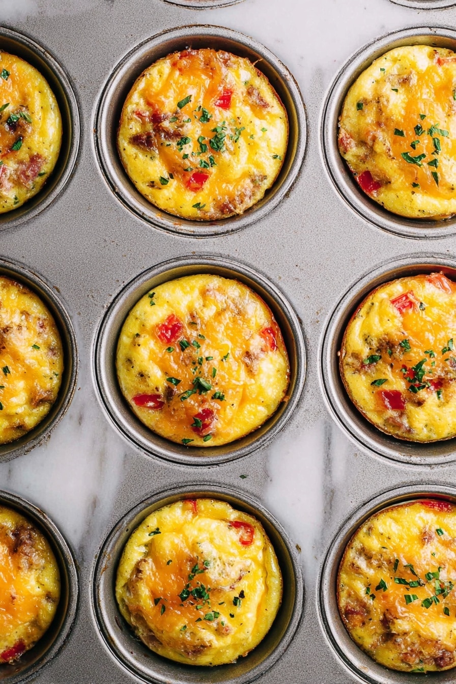 The image shows a close-up of a metal muffin tray filled with nine egg muffins. Each muffin has a golden yellow base with visible pieces of red bell pepper and bits of cooked meat mixed inside. The top surface of each muffin has melted cheese bubbling and slightly browned, with small green herb leaves sprinkled on them. The tray rests on a white marbled surface, showing slight texture and wear. The egg muffins sit neatly in each round muffin cup, with even and rounded tops, each garnished similarly with herbs. photo taken with an iphone --ar 2:3 --v 7 - Hash Brown Egg Cups, Hash Brown Egg Cups recipe, breakfast egg cups, cheesy bacon breakfast cups, easy brunch recipes
