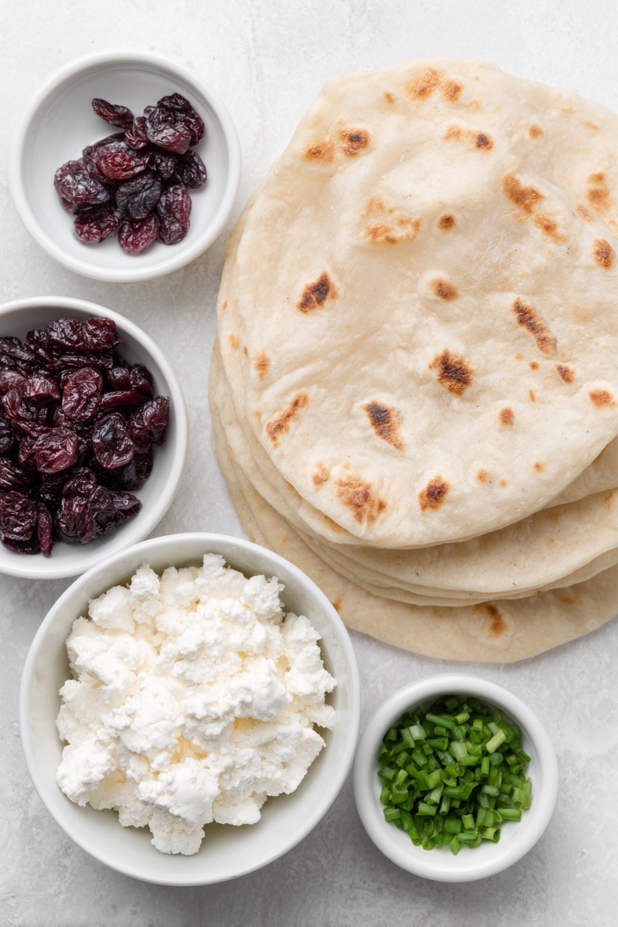 Flat lay of crumbled sheep’s milk feta cheese in a small white ceramic bowl, softened cream cheese in a small white ceramic bowl, sweetened dried cranberries scattered naturally, four whole large flour tortillas stacked neatly, chopped fresh chives in a small white ceramic bowl, all arranged with perfect symmetry and balanced proportions placed on a clean white marble surface, soft natural light, photo taken with an iPhone, professional food photography style, fresh ingredients, white ceramic bowls, no bottles, no duplicates, no utensils, no packaging --ar 2:3 --v 7 --p m7354615311229779997 - Cranberry Feta Roll-Ups, cranberry feta appetizer, holiday snack ideas, easy savory roll-ups, festive appetizer recipes