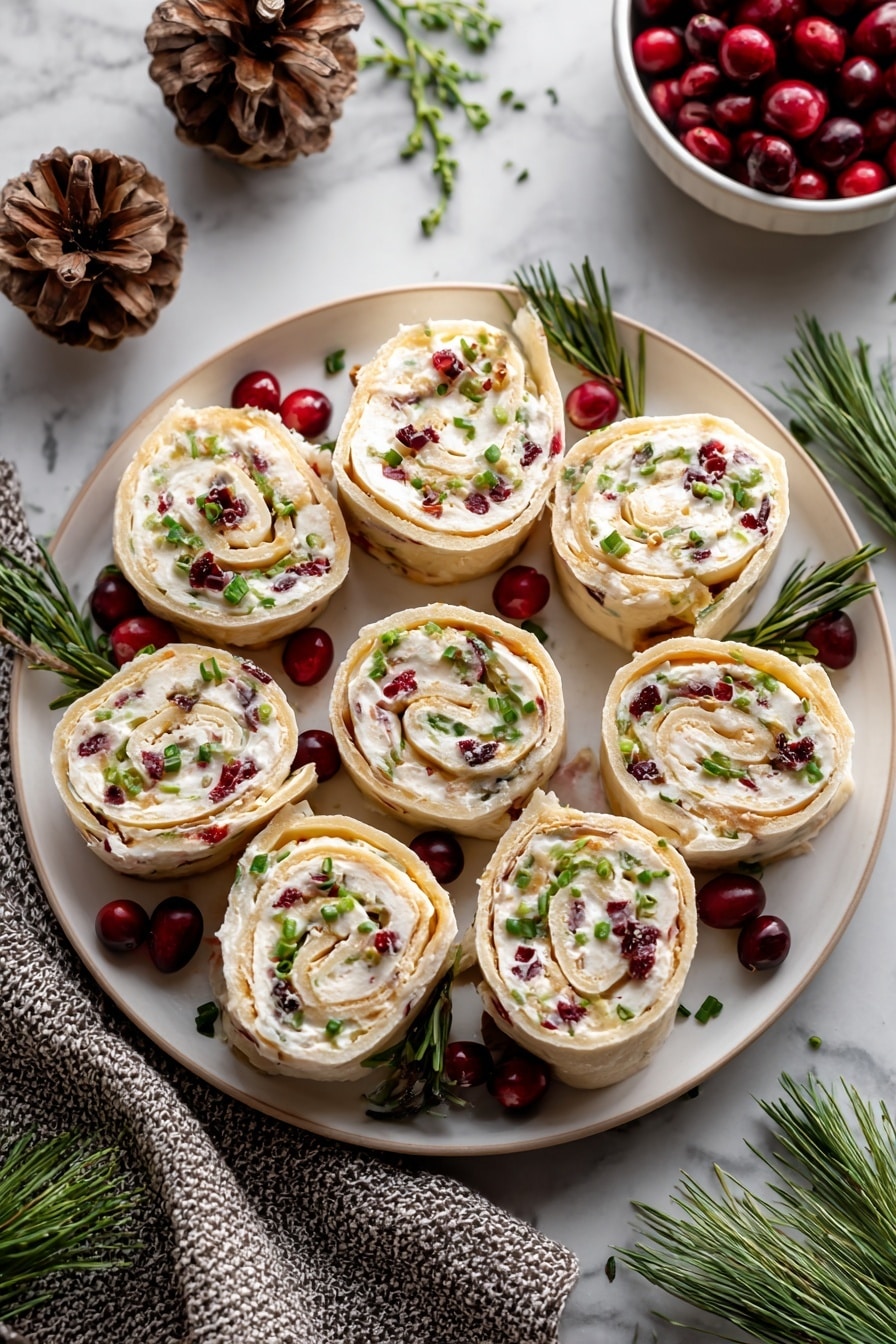 The dish shows eight rolled pinwheel slices on a round white plate, each slice revealing multiple layers of light beige wrap and creamy white filling mixed with small red cranberry bits and green chive pieces on top. The pinwheels are arranged in a circular pattern with extra whole red cranberries and green pine sprigs placed around them for decoration. The plate sits on a white marbled surface with pinecones, a textured gray cloth, and a small white bowl of cranberries nearby enhancing the festive setting. Photo taken with an iphone --ar 2:3 --v 7 - Cranberry Feta Roll-Ups, cranberry feta appetizer, holiday snack ideas, easy savory roll-ups, festive appetizer recipes