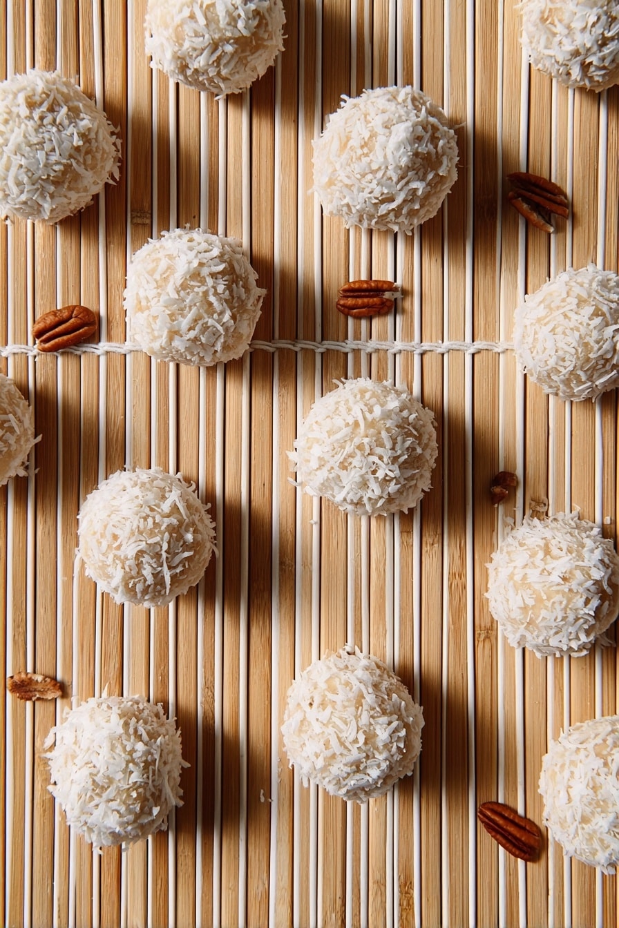 The image shows multiple round balls covered with white coconut flakes arranged on a light bamboo matt with parallel white strings running vertically. The balls have a beige base visible through the coconut flakes and are scattered evenly across the frame. There are small pecan nuts placed randomly around the balls, adding a brown color contrast to the scene. The overall look is clean with a natural, textured feel. Photo taken with an iphone --ar 2:3 --v 7 - Orange Coconut Snowballs, tropical citrus treats, no-bake dessert bites, easy coconut confections, citrus coconut sweets