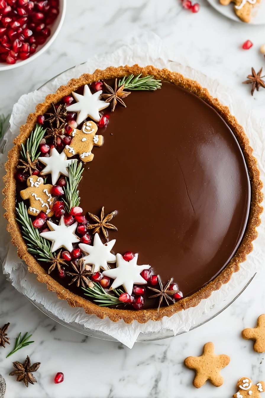 This image shows a round tart with a smooth, shiny chocolate filling, having a golden-brown crust around the edges. The tart is decorated on one side with various small items: white star-shaped cookies with a smooth icing layer, small gingerbread men cookies with white icing details, bright red pomegranate seeds, green rosemary sprigs, and brown star anise pods. The decorations form a thick curved line along one edge of the tart. The tart sits on a white paper on top of a clear glass plate, all placed on a white marbled surface. Nearby, more star-shaped cookies and pomegranate pieces are scattered lightly. Photo taken with an iphone --ar 2:3 --v 7 - Vegan Gingerbread Chocolate Tart, plant-based holiday desserts, festive vegan desserts, gingerbread chocolate tart, dairy-free chocolate tart recipe