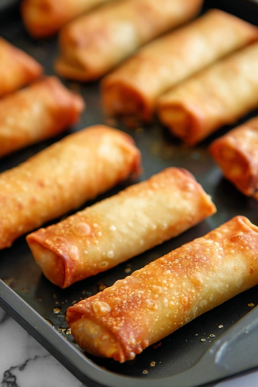 Crispy Oven Baked Egg Rolls Recipe 6 The image shows several golden brown egg rolls placed on a black baking tray with a few small spots of oil around them. Each egg roll is cylindrical with a crispy texture, highlighted by bubbles and slight browning on the surface. The edges are neatly rolled and sealed, showing a slight overlap of the thin dough layer. The egg rolls are arranged in rows, with three in the foreground sharply in focus, while the background rolls are slightly blurred. The whole scene is set on a white marbled surface. photo taken with an iphone --ar 2:3 --v 7 - Crispy Oven Baked Egg Rolls, baked egg rolls, crispy egg rolls, healthy egg roll recipe, oven-baked appetizer
