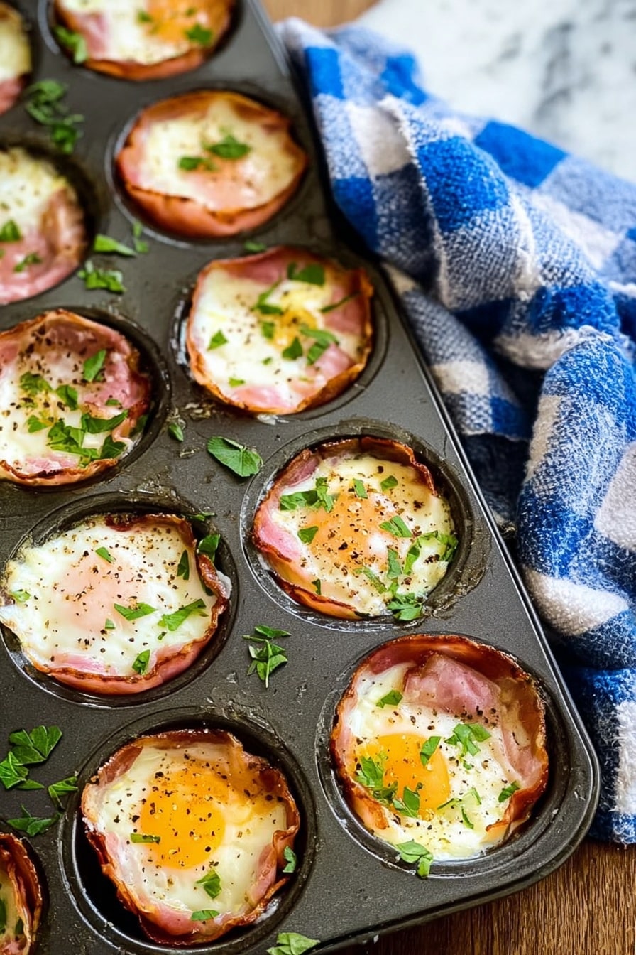 The image shows a dark metal muffin tray filled with baked egg cups, each made with a layer of pinkish ham lining the cup, topped with cooked white eggs that have slightly browned edges and soft yellow yolks in the center, sprinkled with black pepper and small chopped green herbs. The egg cups are arranged in a 3 by 4 grid in the tray. The tray rests on a wooden surface with a blue and white checkered cloth draped nearby, and the background is a white marbled texture. Photo taken with an iphone --ar 2:3 --v 7 - Ham and Egg Breakfast Cups, easy breakfast recipes, quick breakfast ideas, brunch recipe, savory breakfast cups