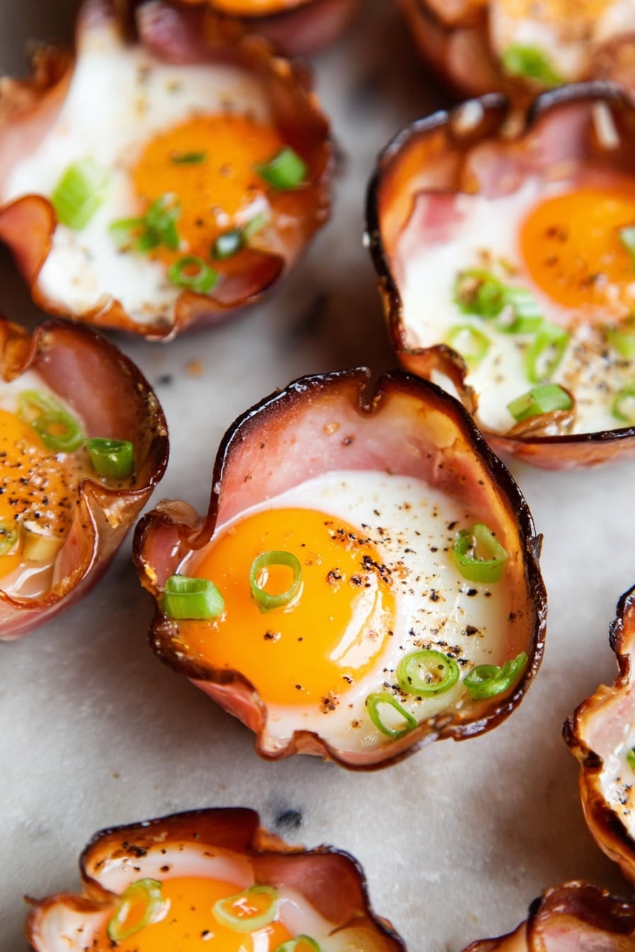 Ham and Cheese Egg Cups Recipe 6 The image shows several small cups made from thin slices of cooked ham, each cup holding a cooked egg. Each egg has a bright yellow yolk in the center with white surrounding it. The edges of the ham cups are slightly crispy and darkened. Small green onion slices are scattered on top of the eggs for garnish, and there is some ground black pepper sprinkled over the yolks and whites. The cups are placed close together on a flat surface with a white marbled texture. photo taken with an iphone --ar 2:3 --v 7 - Ham and Cheese Egg Cups, easy breakfast egg cups, quick brunch recipes, healthy egg muffin cups, savory egg cup ideas