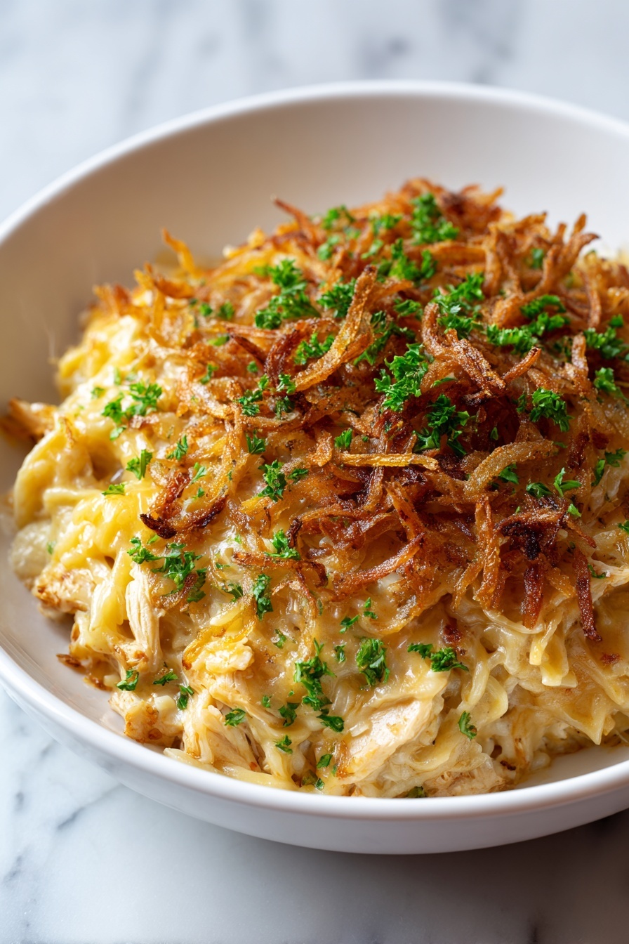 A white bowl holds a creamy, pale yellow noodle dish with three layers visible: the base layer of soft noodles mixed with chunks of chicken, the middle melted cheese layer that is slightly golden and stringy, and the top layer of crispy, dark golden-brown fried onions scattered all around. Small fresh green parsley pieces are sprinkled evenly on top, adding a bright contrast to the rich colors. The bowl sits on a white marbled surface with soft natural lighting. Photo taken with an iphone --ar 2:3 --v 7 - French Onion Chicken Orzo Bake, cheesy chicken pasta bake, caramelized onion casserole, one-pan chicken orzo recipe, comfort food chicken bake