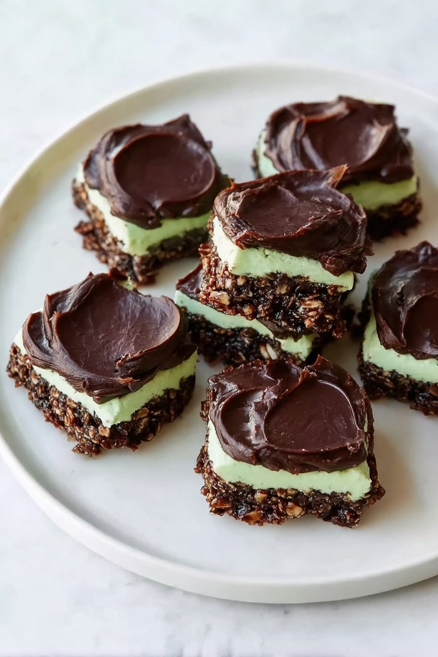 Fudgy Mint Chocolate No-Bake Cookies Recipe 8 The image shows a white plate with eight square-shaped treats arranged loosely on its surface, sitting on a white marbled background. Each treat has three distinct layers: a bottom layer made of a dark, chunky, chocolatey mixture with a rough texture, a middle thin layer of smooth light green cream, and a top thick layer of dark chocolate spread with a glossy, slightly uneven surface. The treats vary slightly in shape but mostly appear square with rounded edges. The lighting is bright and natural, highlighting the shiny top layer and the creamy middle layer. Photo taken with an iphone --ar 2:3 --v 7 - Fudgy Mint Chocolate No-Bake Cookies, mint chocolate cookies, no-bake chocolate mint treats, quick mint chocolate desserts, fudgy cookie recipes
