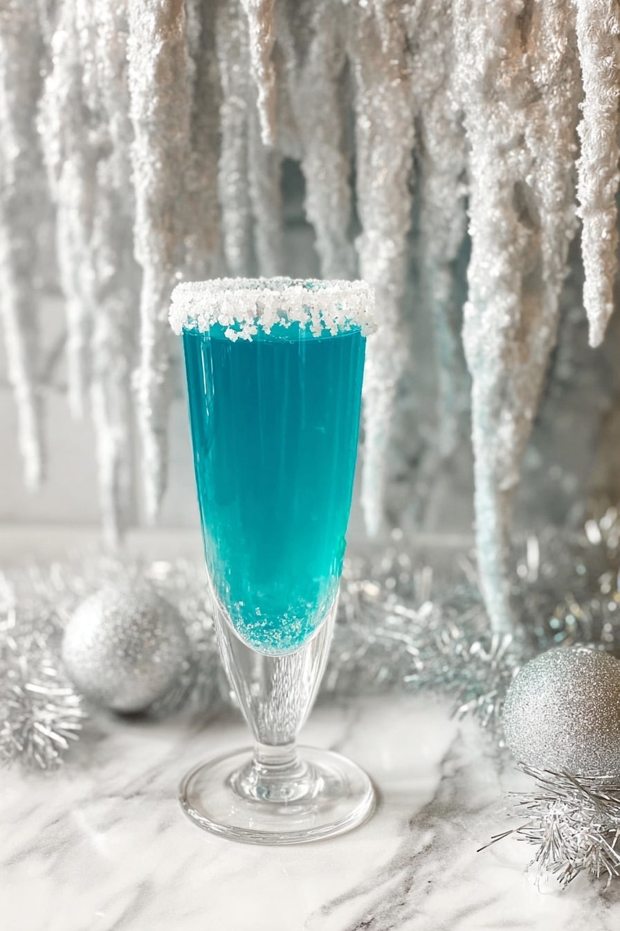 Blue Curacao Mimosa Recipe 6 A tall clear glass filled with bright blue liquid, with a single layer of thick white sugar crystals rimmed around the top edge. The glass stands on a white marbled surface, surrounded by white shimmering tinsel. Behind the glass hangs a large decoration resembling white icicles with a glittery, icy texture, adding a frosty winter feel. The photo taken with an iphone --ar 2:3 --v 7 - Blue Curacao Mimosa, Blue Curacao cocktail, tropical brunch drinks, colorful champagne cocktail, vibrant mimosa recipe