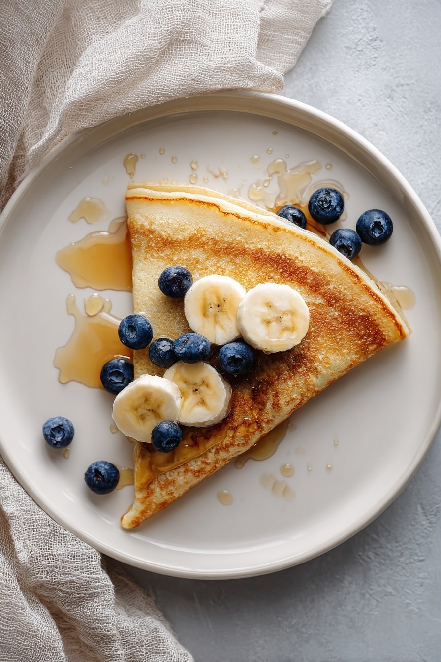 A tall stack of four thick, fluffy light brown pancakes sits on a white plate, with syrup gently dripping down the sides. On top, there are two slices of light yellow banana with soft texture, a few shiny dark blue blueberries, and dollops of creamy white whipped cream arranged in a circle around the fruit. More blueberries and banana slices are placed at the base of the pancake stack, resting on the white marbled surface. The syrup catches the light, adding a warm golden shine to the dish. photo taken with an iphone --ar 2:3 --v 7 - Banana Pancakes, Easy Banana Pancake, Fluffy Banana Pancakes, Quick Banana Breakfast, Ripe Banana Pancake