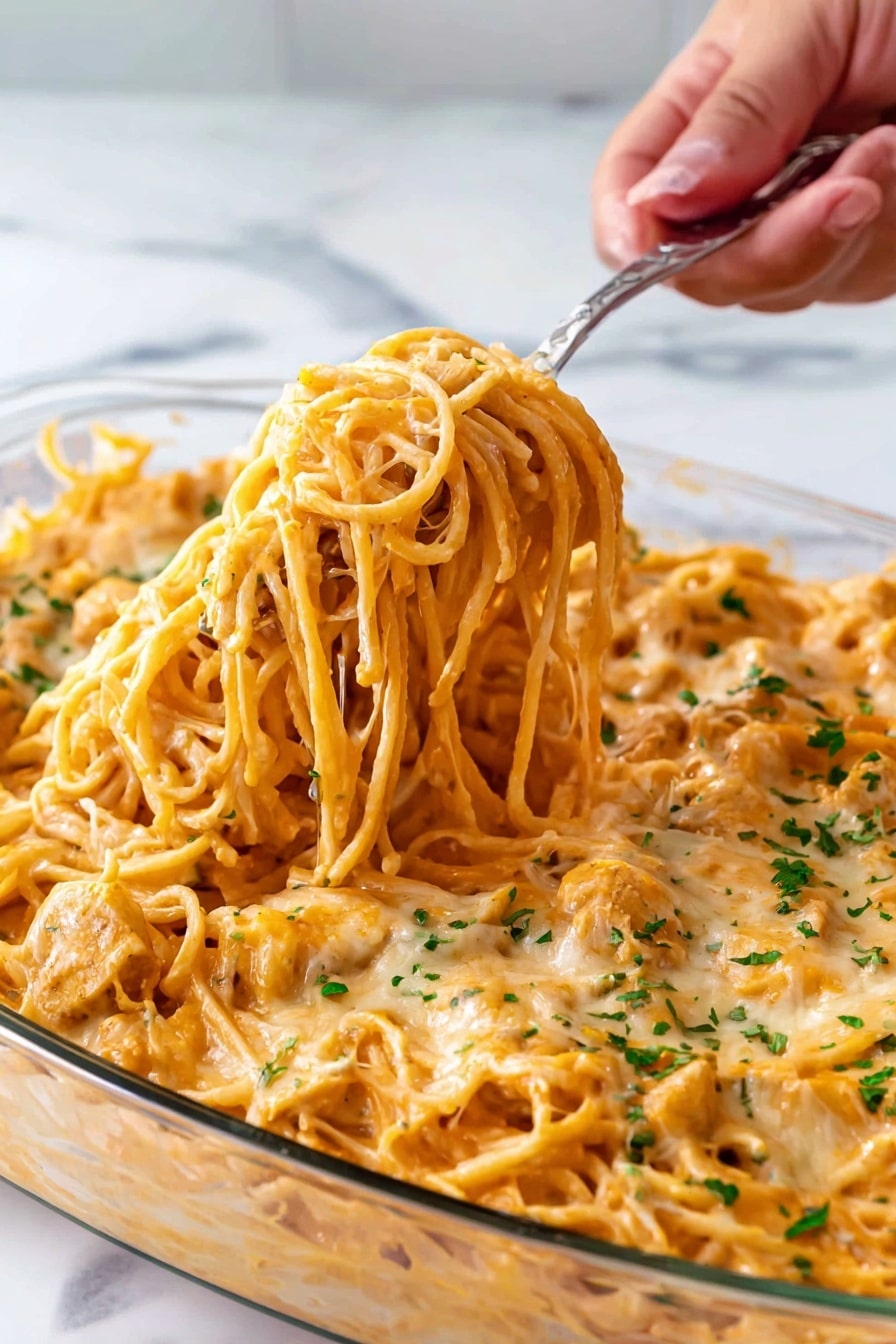 Creamy Chicken Spaghetti Bake Recipe 6 A clear glass dish filled with creamy orange spaghetti noodles layered with melted cheese and small pieces of chicken, topped with chopped green herbs. A woman's hand is using a silver fork to lift a thick bunch of the spaghetti from the dish, showing the noodles coated in sauce and cheese. The dish sits on a white marbled surface. photo taken with an iphone --ar 2:3 --v 7 - Creamy Chicken Spaghetti Bake Chicken Spaghetti Bake Easy comfort food cheesy pasta casserole creamy pasta dish family favorite