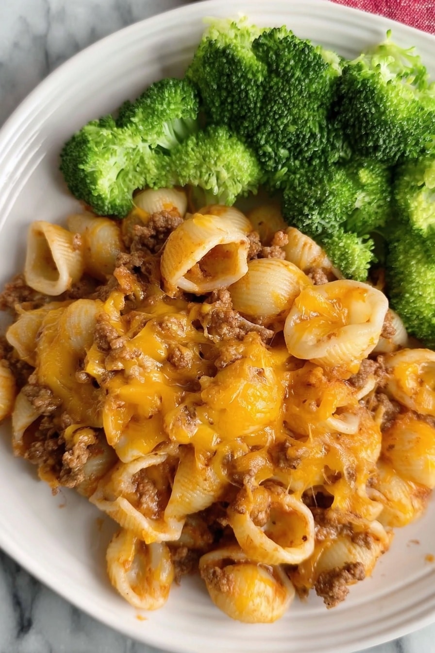 Easy Ground Beef Pasta Casserole Recipe 6 The dish shows a plate filled with three layers: the bottom layer is small pasta shells mixed with cooked ground meat that is soft brown in color; the middle layer is melted cheddar cheese with an orange and golden-brown texture spread evenly over the pasta, giving it a slightly crispy look in places; the top layer is bright green broccoli florets placed on one side of the plate. The plate is white, and the surface beneath is white marble. Photo taken with an iphone --ar 2:3 --v 7 - Easy Ground Beef Pasta Casserole, ground beef pasta bake, cheesy beef casserole, quick dinner ideas, hearty family meal