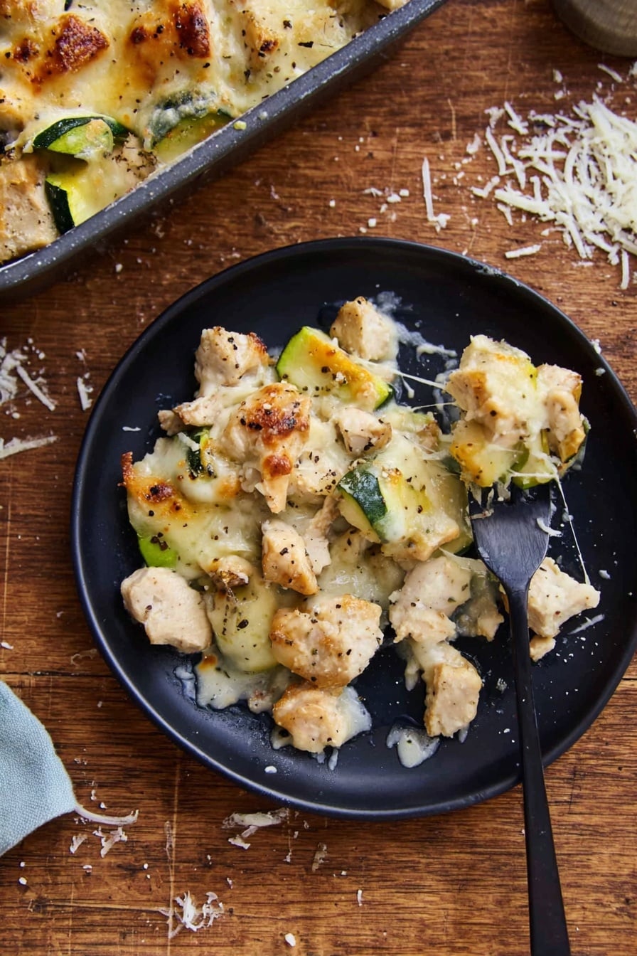 Easy Chicken Zucchini Casserole Recipe 6 The image shows a black round plate with a serving of a baked dish made of three main visible layers. The bottom layer consists of small, uneven pieces of light beige chicken mixed with chunks of green zucchini. The middle layer is melted light golden cheese, spread unevenly, some parts browned slightly. Scattered black pepper flakes are visible on top. A black fork on the right side of the plate holds a piece of chicken and zucchini, with cheese strands stretching between the fork and plate. The plate is placed on a wooden surface with some grated white cheese scattered nearby. A covered baking dish with extra portions of the same dish is partly visible in the top left. The photo taken with an iphone --ar 2:3 --v 7 - Easy Chicken Zucchini Casserole, healthy chicken zucchini bake, quick zucchini casserole, cheesy chicken zucchini recipe, family-friendly zucchini casserole