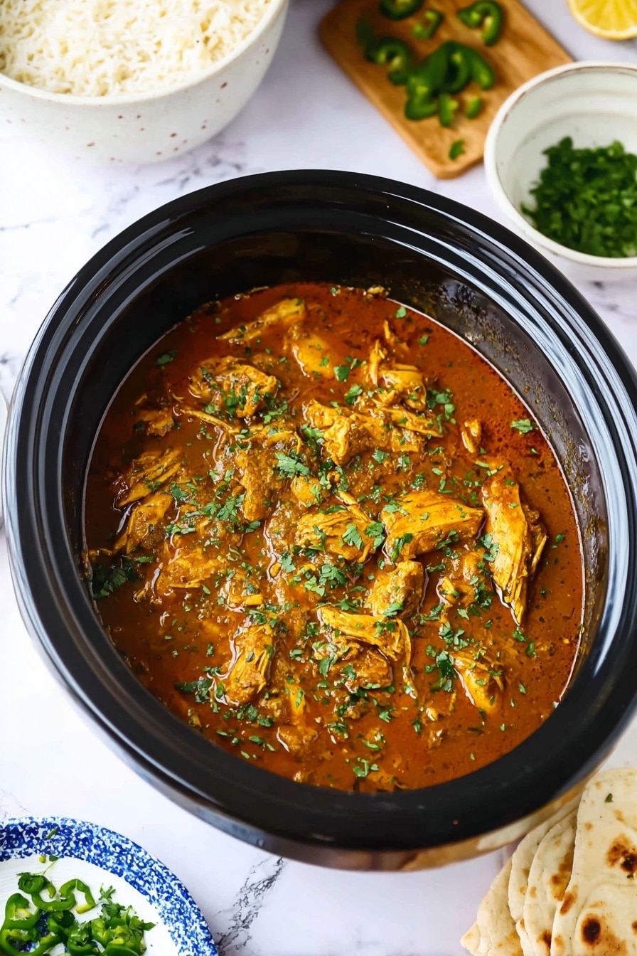 Easy Slow Cooker Chicken Curry Recipe 8 A close-up image of a black slow cooker filled with brown chicken curry topped with chopped green herbs, showing pieces of chicken submerged in a thick sauce. Surrounding it, on a white marbled surface, there is a white bowl with white rice on the top left, a wooden board with chopped green peppers on the top right, a small white bowl with chopped herbs on the bottom left, and a blue and white plate with flatbread on the bottom right. The scene is bright and fresh, highlighting the colors and textures of the curry and sides. photo taken with an iphone --ar 2:3 --v 7 - Easy Slow Cooker Chicken Curry, slow cooker chicken curry, chicken curry recipe, flavorful chicken curry, simple slow cooker dinner