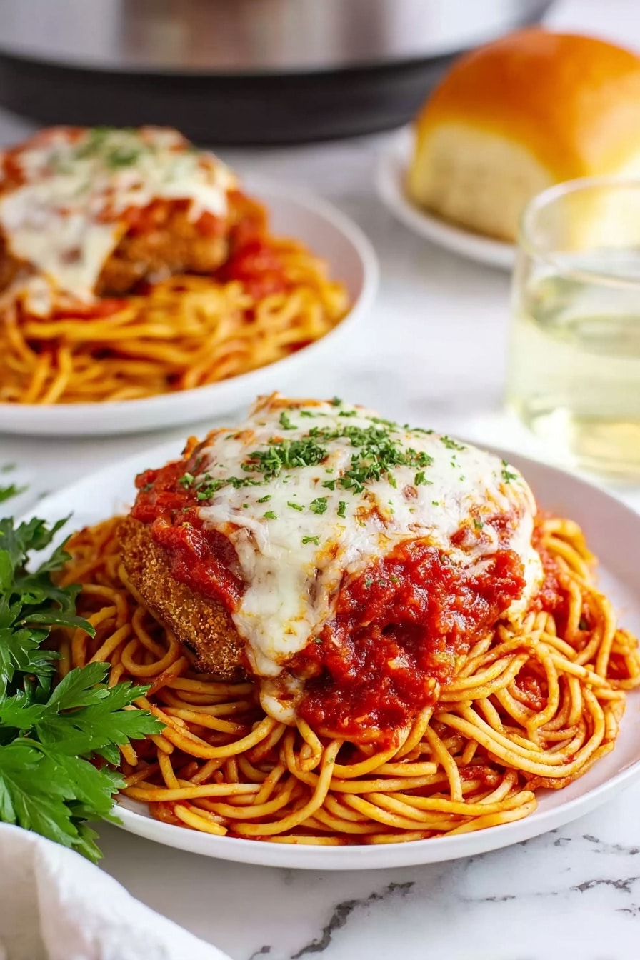 Slow Cooker Chicken Parmesan Recipe 8 A white plate holds a layered dish starting with a base of thin spaghetti noodles coated in bright red tomato sauce, arranged in a round nest shape. On top of the noodles lies a large breaded and fried meat cutlet covered with melted white cheese and more chunky red tomato sauce sprinkled with small green parsley bits. A sprig of fresh green parsley rests beside the plate on a white marbled surface. In the background, a second white plate holds the same dish, a glass of clear liquid, and a round golden bread roll. photo taken with an iphone --ar 2:3 --v 7 - Slow Cooker Chicken Parmesan, Chicken Parmesan recipe, easy slow cooker chicken dishes, cheesy chicken dinner, fuss-free chicken parmesan
