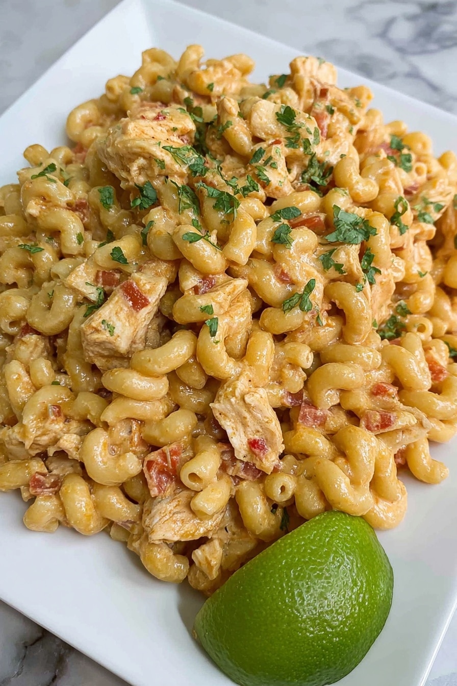 Creamy Chicken Enchilada Pasta Recipe 6 A plate of creamy macaroni pasta mixed with pieces of cooked chicken, covered in a light orange sauce with small bits of red tomato, and sprinkled with green herbs on top. The pasta is curly and soft-looking, forming the main thick layer, while the chicken pieces are spread evenly within it. The dish is served on a white square plate, with a bright green lime half placed at the bottom right side. The background is a white marbled surface. Photo taken with an iphone --ar 2:3 --v 7 - Creamy Chicken Enchilada Pasta, Chicken Enchilada Pasta, Easy Creamy Pasta Recipes, Quick Weeknight Dinner, Cheesy Chicken Pasta