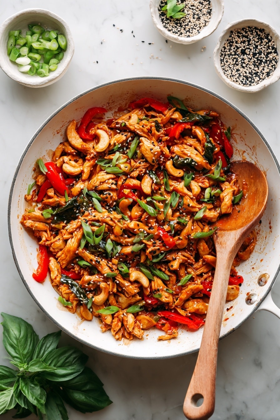 Gochujang Chicken Bowls Recipe 8 A white pan filled with a stir-fry dish that has shredded orange-brown chicken mixed with bright red bell pepper pieces, green basil leaves, and whole cashew nuts. The mixture is glossy with sauce and sprinkled with black and white sesame seeds, plus sliced green onions on top. A wooden spoon rests inside the pan, coated with the same sauce and ingredients. Around the pan, there are small white bowls containing sliced green onions and a mix of black and white sesame seeds on a white marbled surface. Fresh green basil leaves lie at the bottom left corner. photo taken with an iphone --ar 2:3 --v 7 - Gochujang Chicken Bowls, Korean chicken bowls, spicy chicken rice bowls, healthy Korean-inspired bowls, easy Gochujang chicken recipe