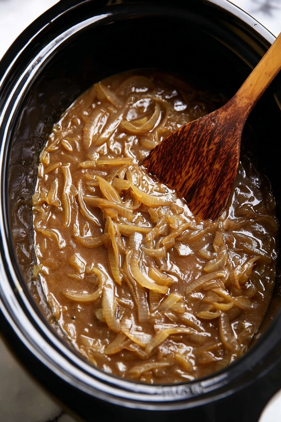 Slow Cooker French Onion Soup Recipe 8 A close-up view inside a black slow cooker filled with soft cooked onions in a thick, brown sauce, showing many translucent, light brown onion slices mixed evenly in a rich, glossy gravy. On the right side, a wooden spoon with a worn, darker brown tip lies partially submerged among the onions. The slow cooker sits on a surface with a white marbled texture. photo taken with an iphone --ar 2:3 --v 7 - Slow Cooker French Onion Soup, French Onion Soup, Crockpot Onion Soup, Easy French Onion Soup, comforting onion soup