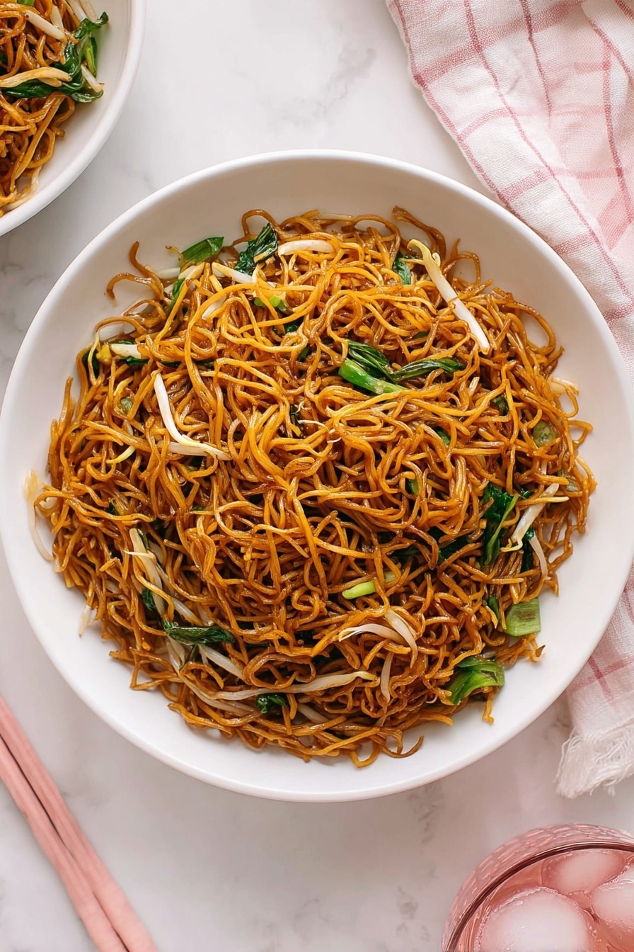 Cantonese Chow Mein Stir Fry Recipe 6 A white shallow bowl is filled with a single layer of dark golden brown fried noodles, with thin light brown bean sprouts and bright green leafy vegetables mixed evenly throughout. The noodles look lightly shiny, tangled, and crispy. The bowl sits on a white marbled surface next to a light pink and white checkered cloth and pink chopsticks, adding soft pastel tones to the image. Part of another white bowl of food and a pink glass with ice are visible at the edges. Photo taken with an iphone --ar 2:3 --v 7 - Cantonese Chow Mein Stir Fry, Cantonese Noodle Stir Fry, Chinese Chow Mein Recipe, Crispy Noodles Stir Fry, Vegetarian Chinese Noodles