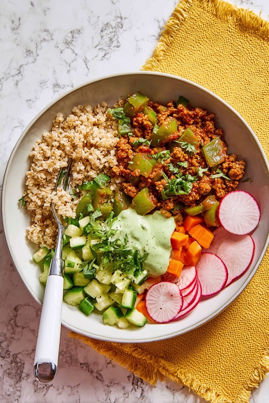 Mediterranean Beef Bowls with Harissa Oil Recipe 6 A white shallow bowl holds a colorful meal divided into four parts. The top left section has light brown cooked grains with a fluffy texture. Below it, there is a saucy mix of minced meat and chopped green bell peppers in a reddish-brown sauce. To the right, a fresh salad section has diced green cucumbers and bright orange carrots covered in a light green creamy dressing. At the bottom right, there are three thin, round slices of radish with white and pink centers. Fresh green herbs are sprinkled on top. A fork with a white handle rests on the edge of the bowl. The bowl sits on a white marbled surface with a yellow fringed cloth nearby. photo taken with an iphone --ar 2:3 --v 7 - Mediterranean Beef Bowls with Harissa Oil, Mediterranean beef bowl recipe, Harissa oil beef bowl, flavorful beef bowls, healthy Mediterranean dinner