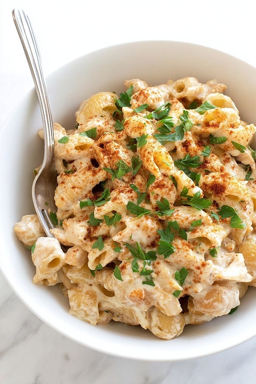 Cajun Chicken Pasta Bake Recipe 8 A white bowl filled with three layers of food, starting with a bottom layer of creamy beige pasta shells mixed with small pieces of light brown chicken. The next layer shows the pasta and chicken coated with a thick creamy sauce that has a light off-white color. The top layer is sprinkled with fresh green parsley leaves and a dusting of reddish-brown spices. A silver fork rests on the left side of the bowl. The background is a white marbled texture. photo taken with an iphone --ar 2:3 --v 7 - Cajun Chicken Pasta Bake, Cajun Chicken Pasta, easy Cajun pasta recipes, creamy Cajun pasta, spicy chicken pasta bake