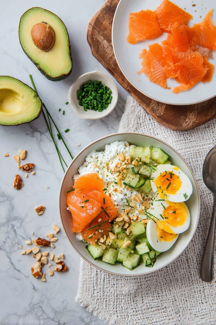 Smoked Salmon and Cottage Cheese Salad Recipe 8 A bowl with a base layer of white cottage cheese topped with four sections: orange smoked salmon slices, cubed green cucumber, sliced avocado, and two halves of a soft-boiled egg with bright yellow yolks. Chopped nuts are sprinkled over the entire bowl along with small green chives. Nearby, a white plate holds extra smoked salmon slices, and a wooden board holds a halved avocado and a small bowl of chopped chives. The setting is on a white marbled surface with a textured white cloth and a metal spoon on the side, scattered with chopped nuts and chives. Photo taken with an iphone --ar 2:3 --v 7 - Smoked Salmon and Cottage Cheese Salad, smoked salmon salad, healthy salmon salad, quick seafood salad, easy cottage cheese salad