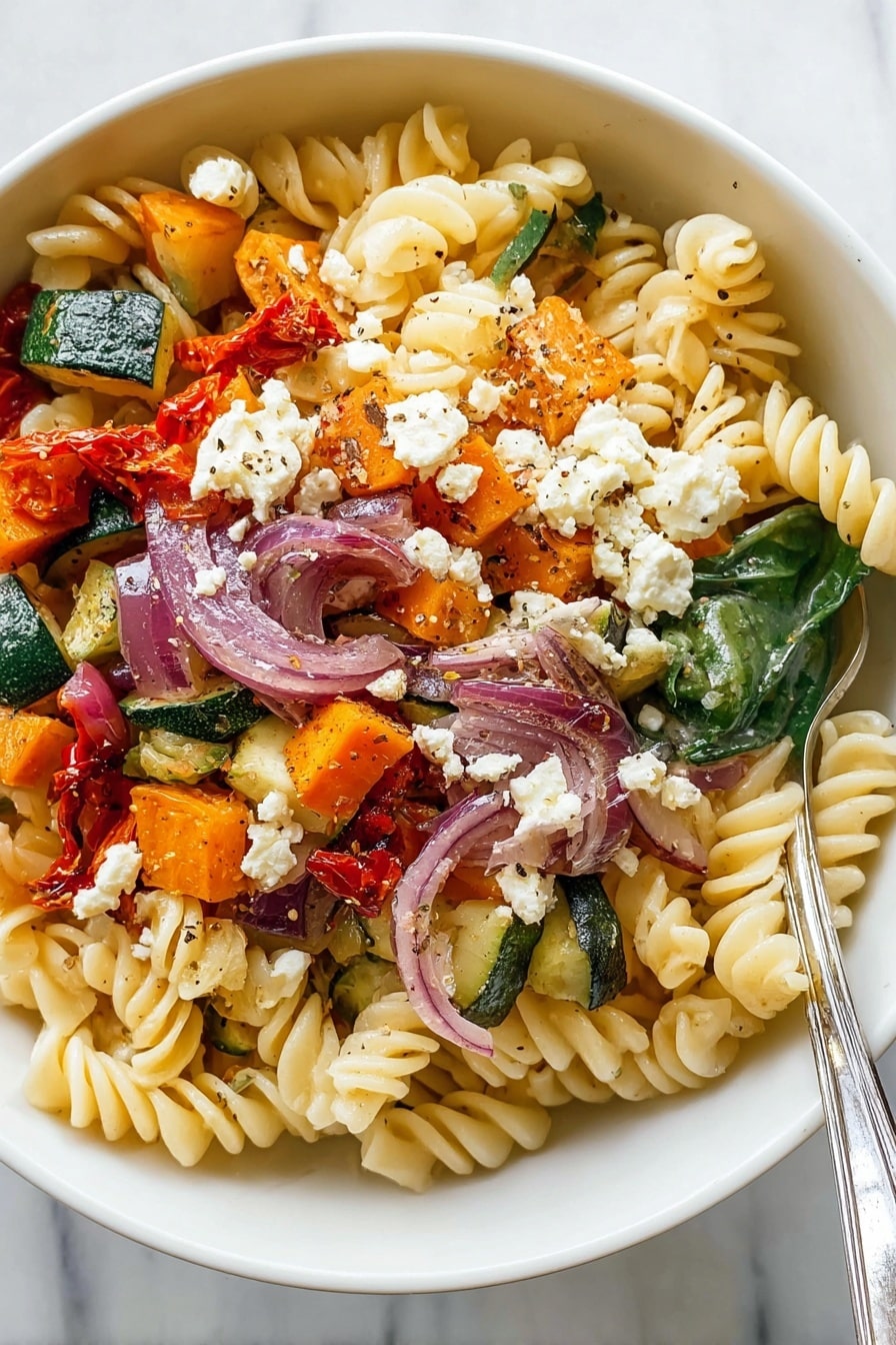 Roasted Veggie Pasta with Feta Recipe 6 The image shows a bowl of pasta salad with three main layers. At the base, there is a layer of light yellow spiral pasta with a soft texture. On top of the pasta, there are colorful vegetables scattered: green zucchini chunks, orange sweet potato pieces, slices of red onions, and some wilted spinach leaves. The top layer has some crumbled white cheese, small roasted red pepper pieces, and a sprinkle of black pepper for seasoning. The bowl is white and the surface background has a white marbled texture. A silver fork rests inside the bowl on the right side. Photo taken with an iphone --ar 2:3 --v 7 - Roasted Veggie Pasta with Feta, roasted vegetable pasta, feta pasta recipe, quick healthy pasta, veggie and feta pasta