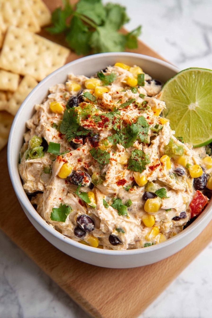 Southwest Chicken Salad Recipe 8 A white bowl filled with a mixed salad showing three main layers: creamy light beige shredded chicken mixed with black beans and yellow corn kernels as the first layer, small bits of red pepper and green celery pieces throughout the second layer, and fresh chopped green cilantro sprinkled on top with a dusting of red spice. A single bright green lime wedge leans on the side inside the bowl. The bowl is placed on a light brown wooden board against a white marbled surface. Photo taken with an iphone --ar 2:3 --v 7 - Southwest Chicken Salad, Southwest Chicken Salad Recipe, Easy Southwest Chicken Salad, Healthy Southwest Chicken Salad, Quick Chicken Salad